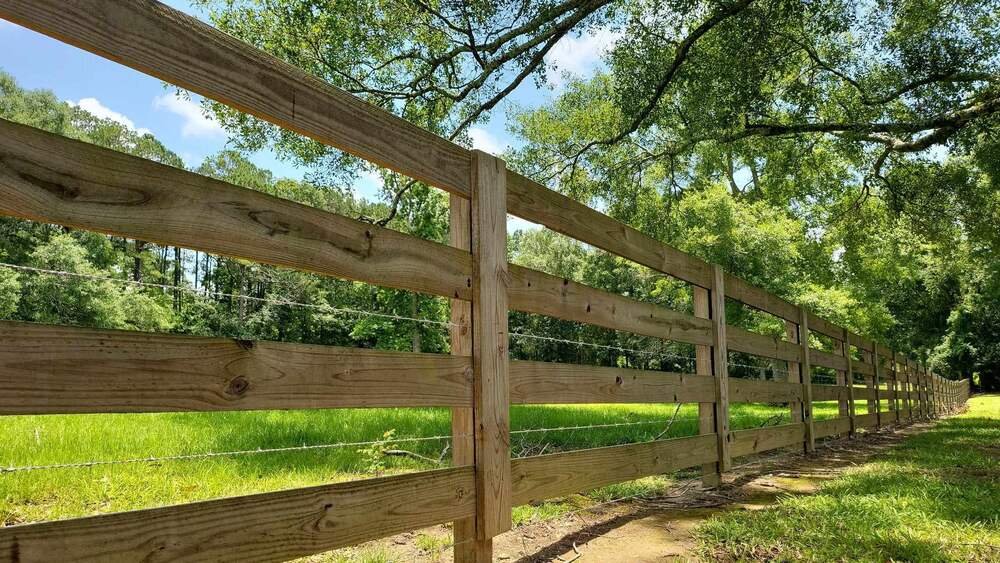 Three-board wood rail fence with wire mesh backing built along a green pasture
